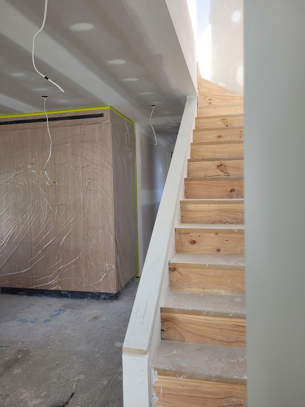 Stair beside timber-veneer wall joinery protected in plastic wrap